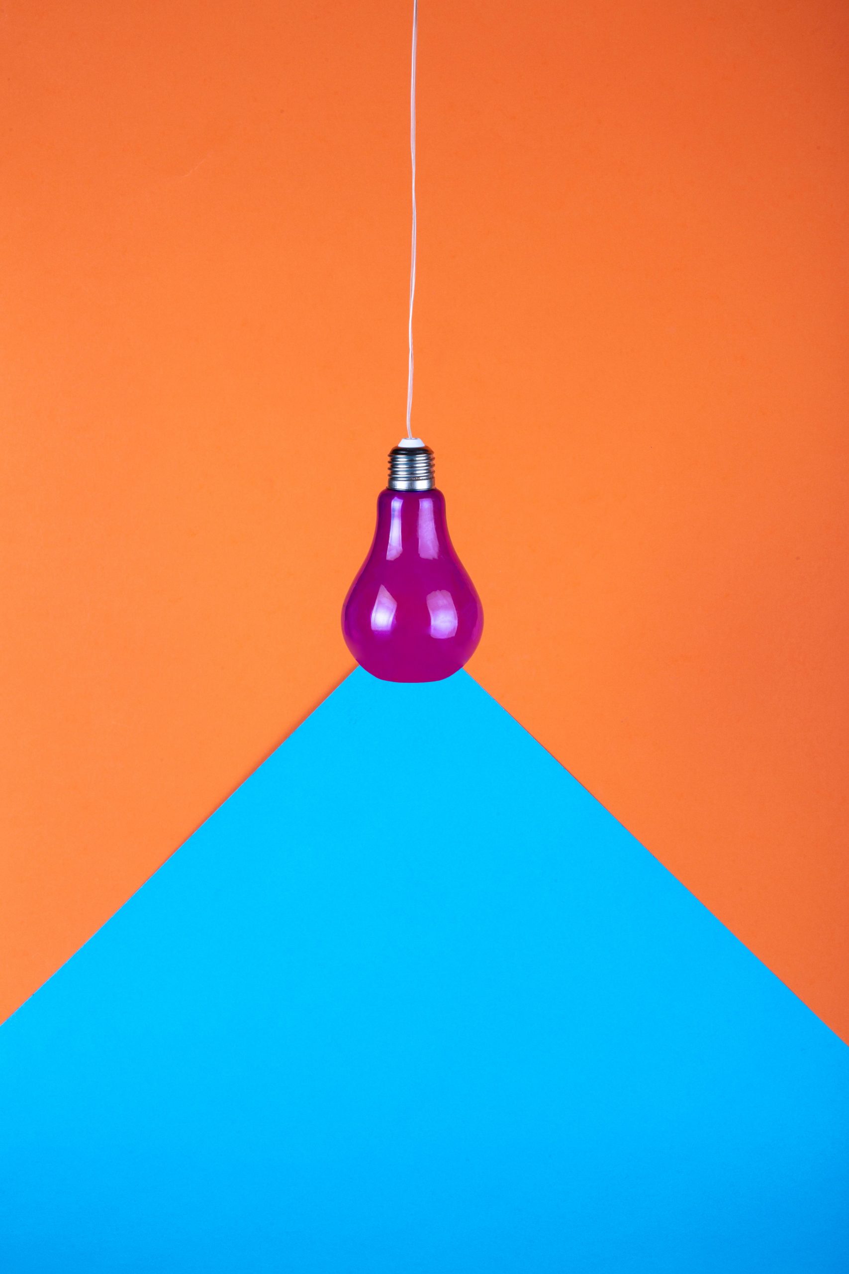 A purple light bulb hanging against an orange and blue geometric split background.