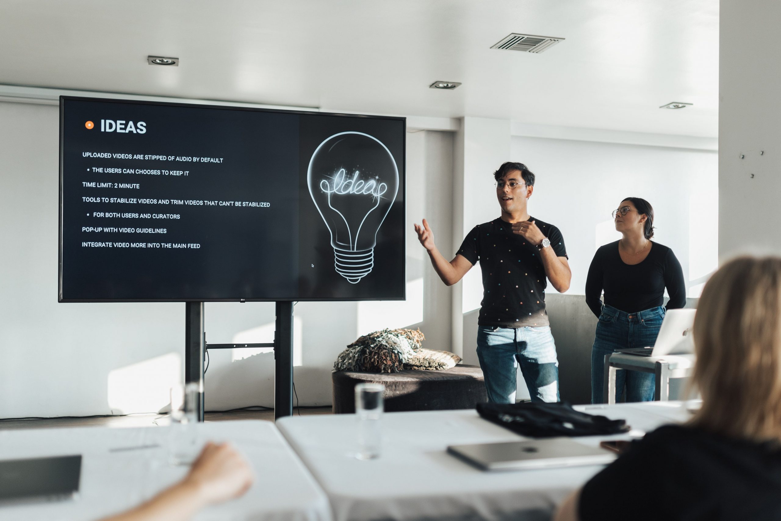 A Presenter pointing to a digital screen displaying product ideas and lightbulb visual during a team meeting